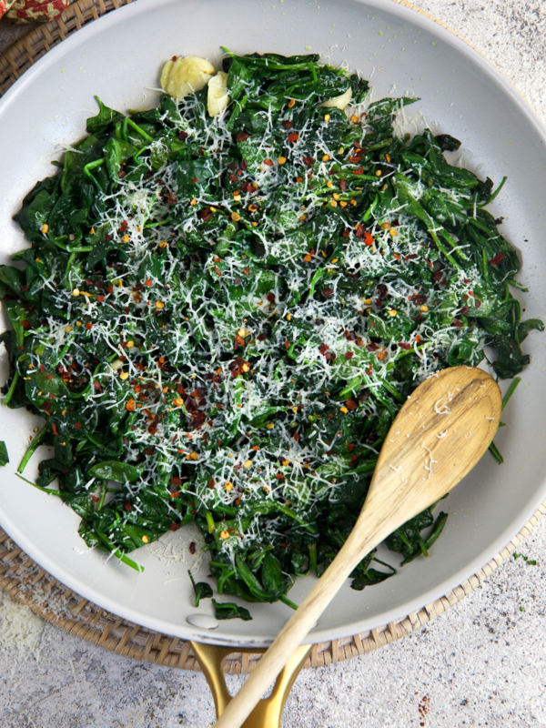 A spoon is placed in a skillet filled with sautéed spinach.