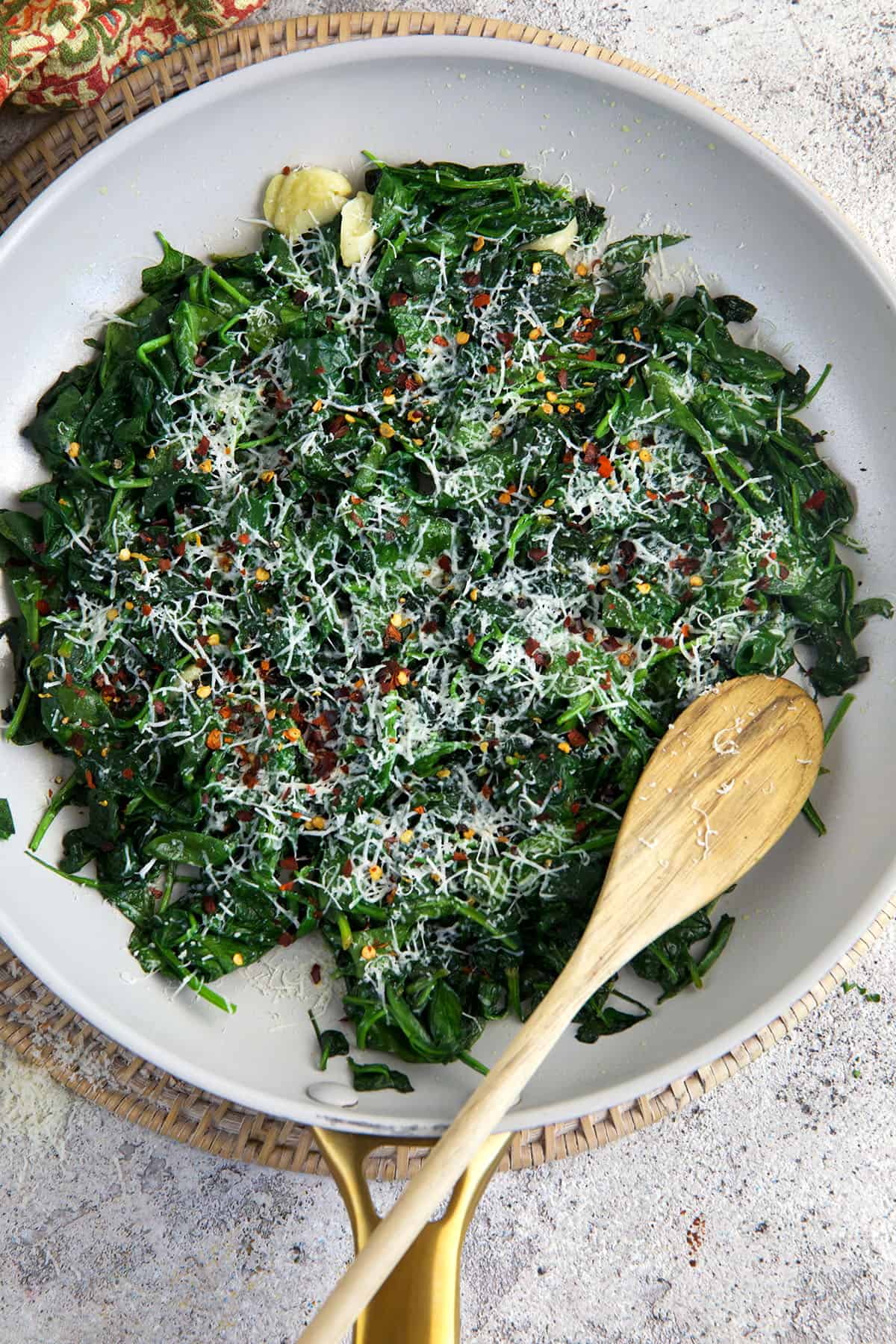A spoon is placed in a skillet filled with sautéed spinach. 
