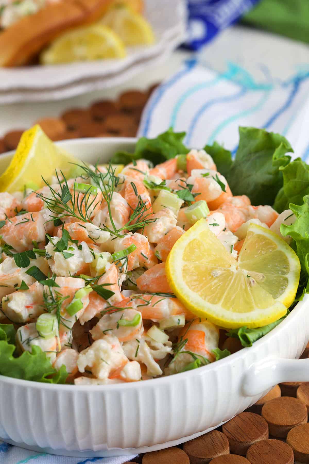 A white bowl is filled with shrimp salad and lemon slices. 