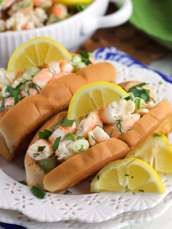 Two shrimp salad rolls are garnished with lemon wedges.