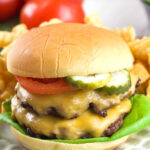 A smash burger is topped with pickles and tomatoes.