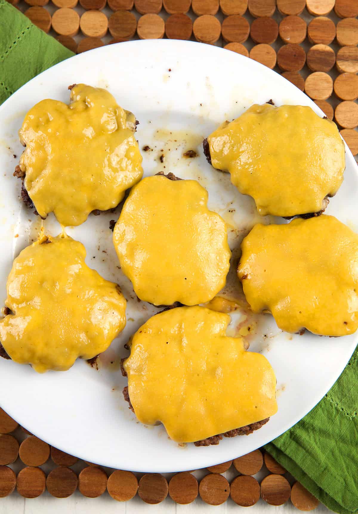 Cheesy burger patties are on a white plate. 