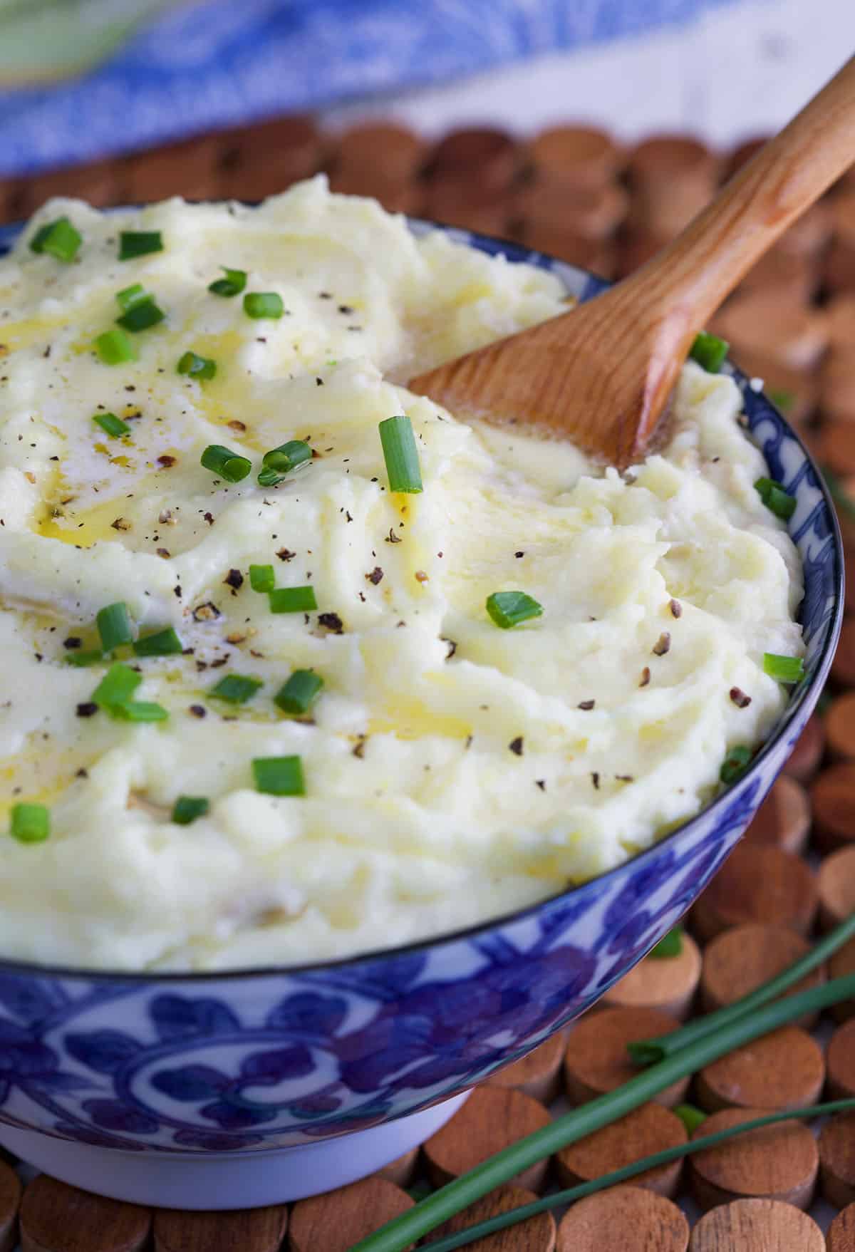 close up of mashed potatoes in a blue serving bowl with a spoon for serving.