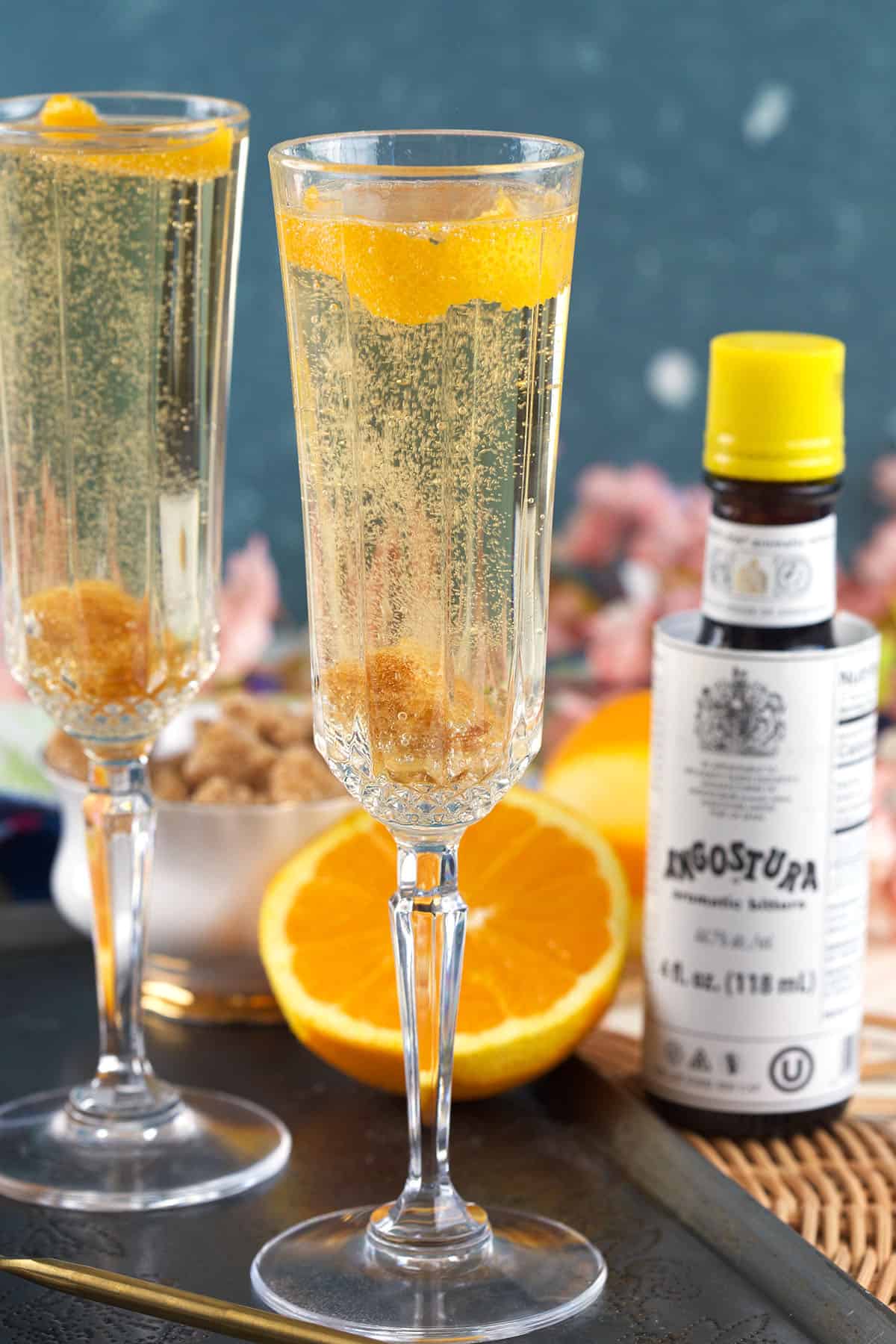 Two glasses of champagne cocktails are placed next to other ingredients. 