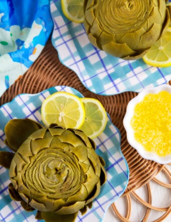 Plated artichokes are placed next to lemon slices.