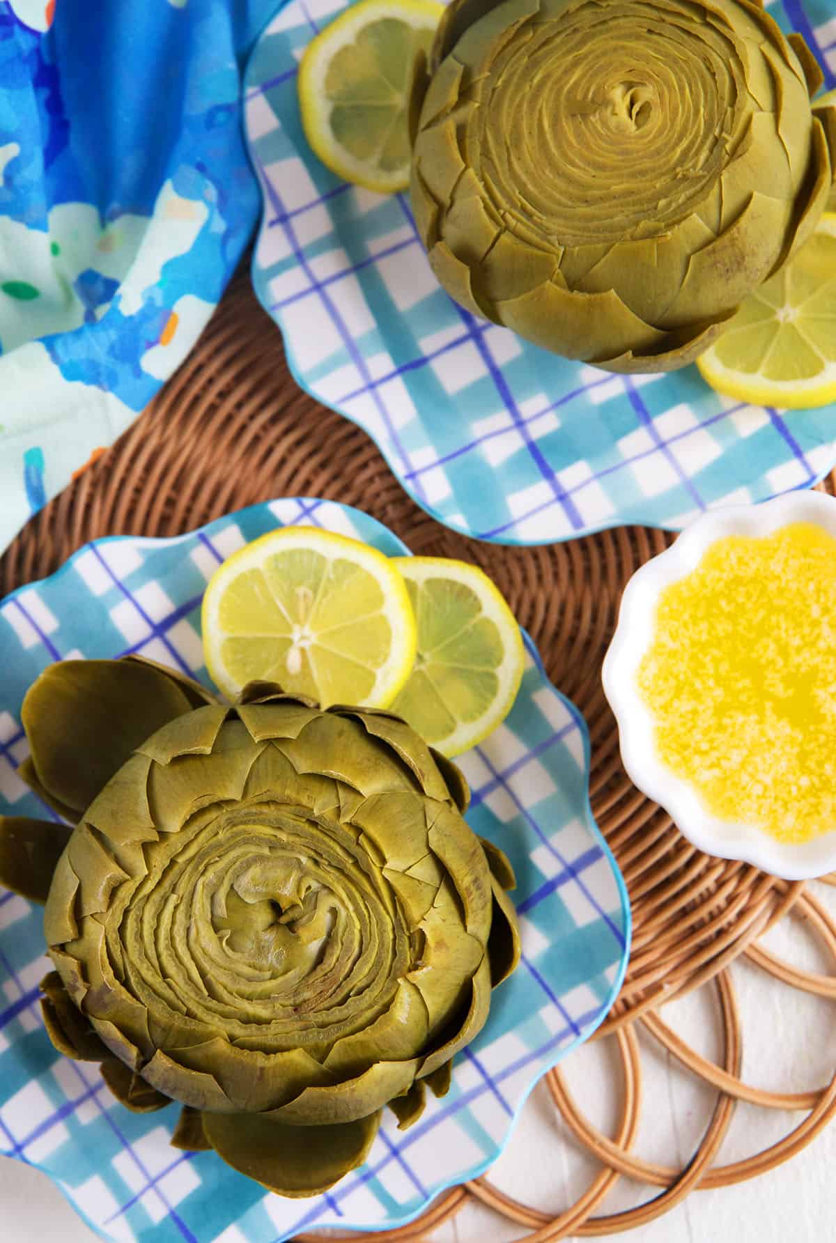 Plated artichokes are placed next to lemon slices. 