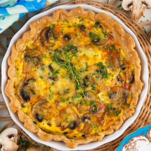 A baked mushroom quiche is garnished with fresh herbs.