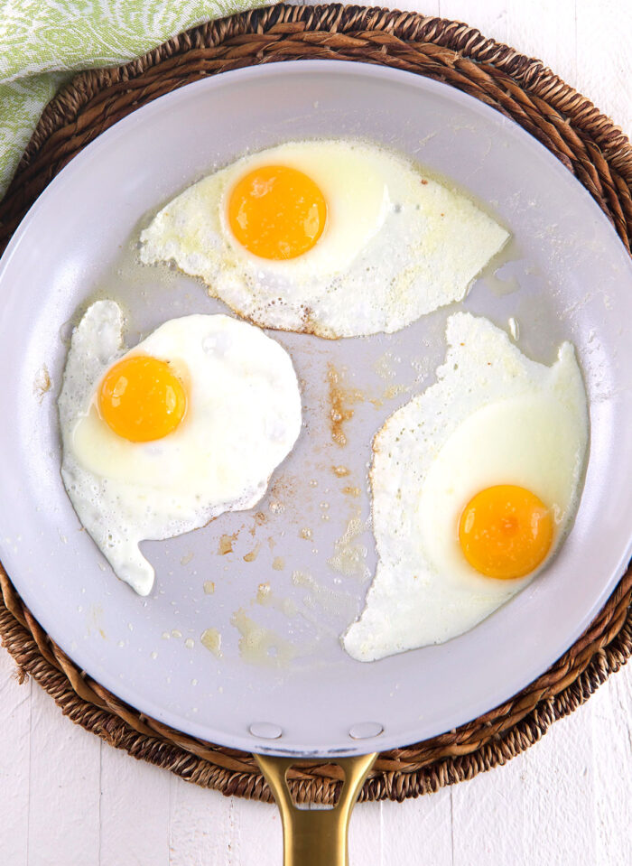 Raw eggs are cooking in a skillet. 