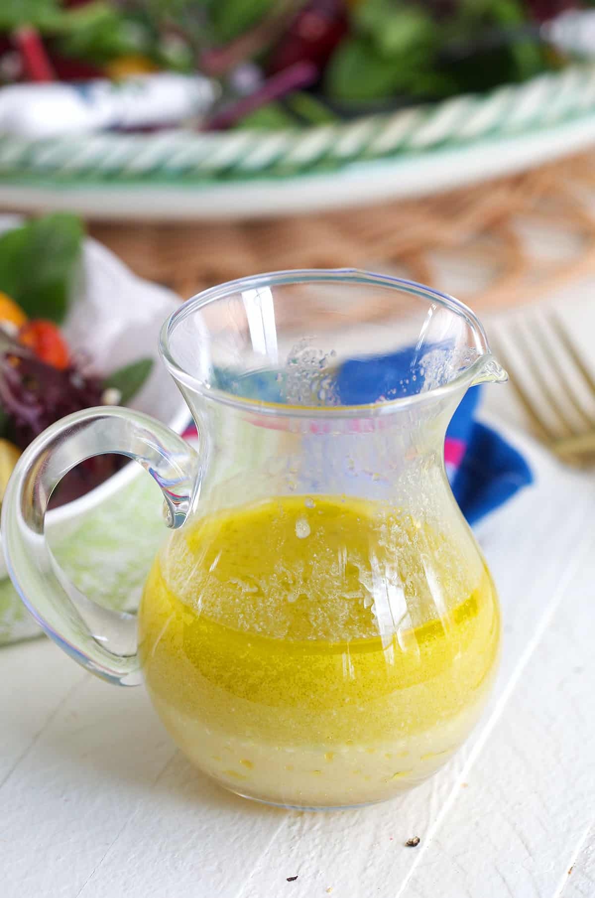 A small glass pitcher is filled with salad dressing. 