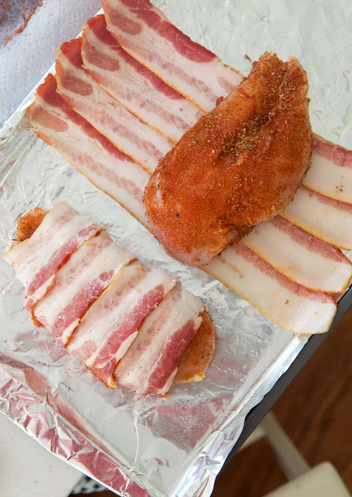 A seasoned chicken breast is placed in the middle of bacon slices. 