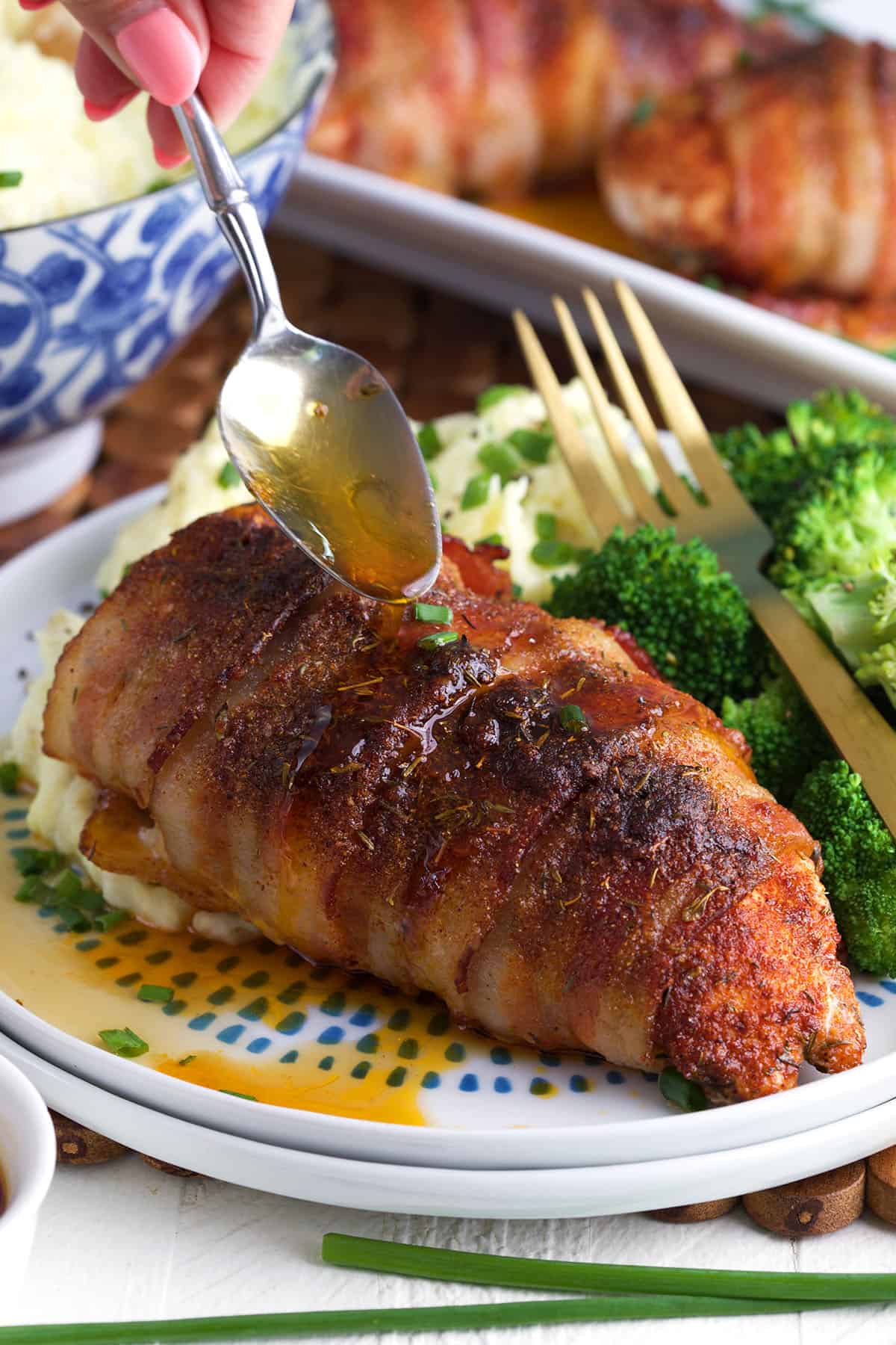 A bacon wrapped chicken breast is being drizzled with pan drippings. 