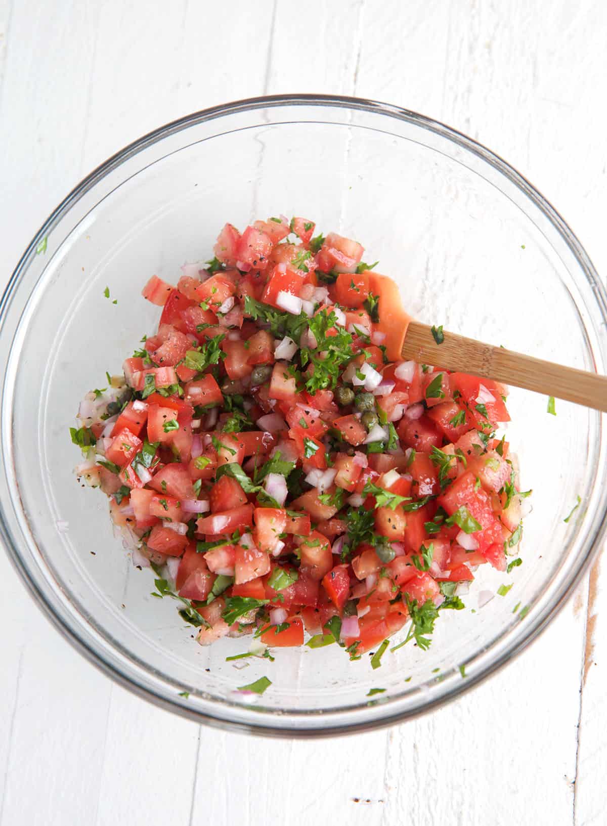 A wooden spoon is mixing together a bruschetta mixture. 