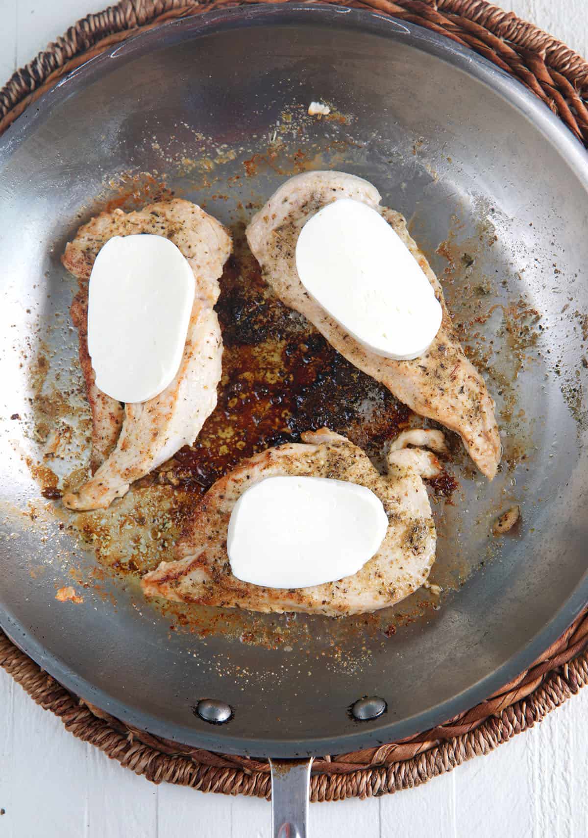 Three pieces of chicken in a skillet are each topped with mozzarella. 