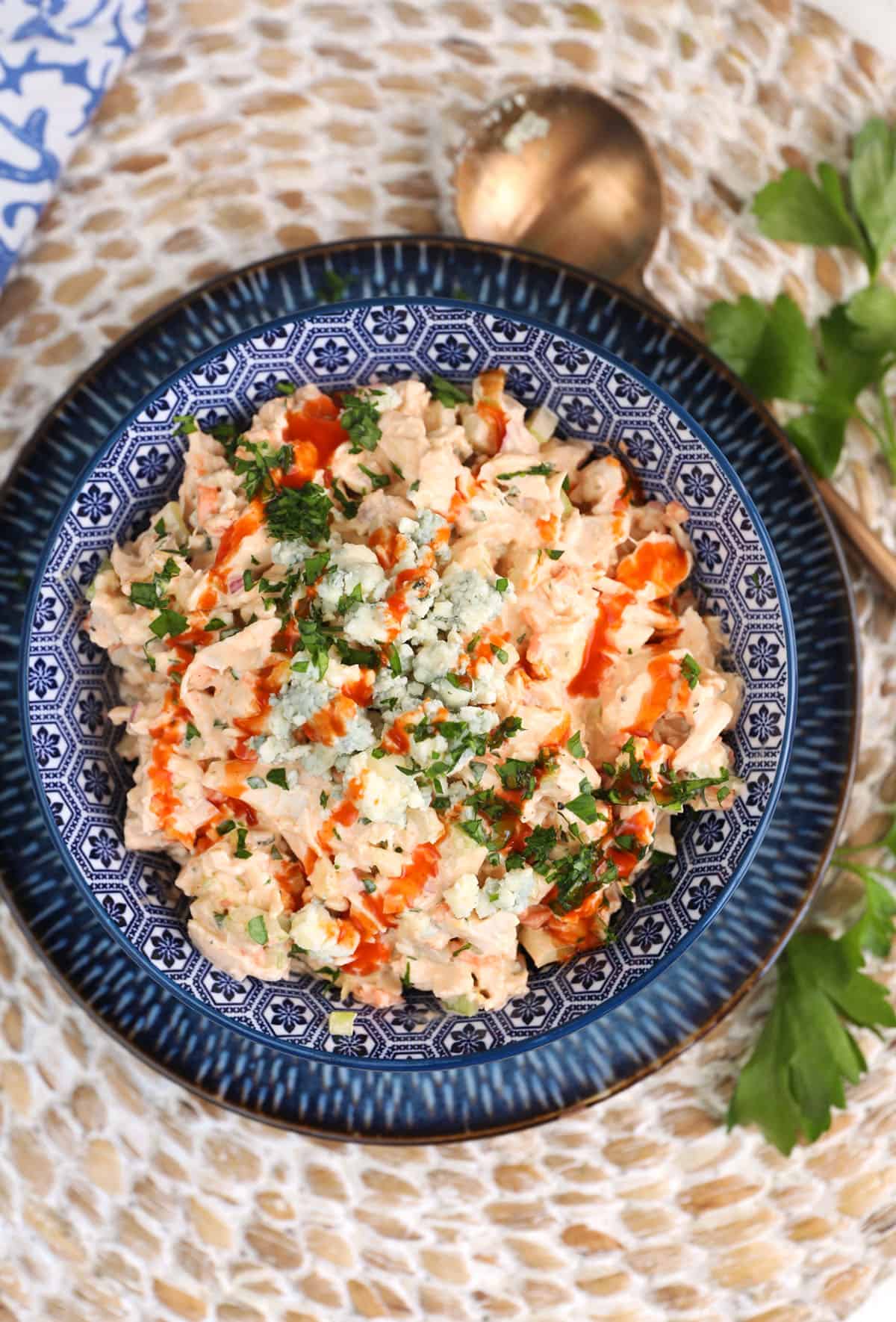 A blue bowl filled with chicken salad is garnished with hot sauce. 