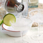 A cocktail is being poured through a strainer into a glass.
