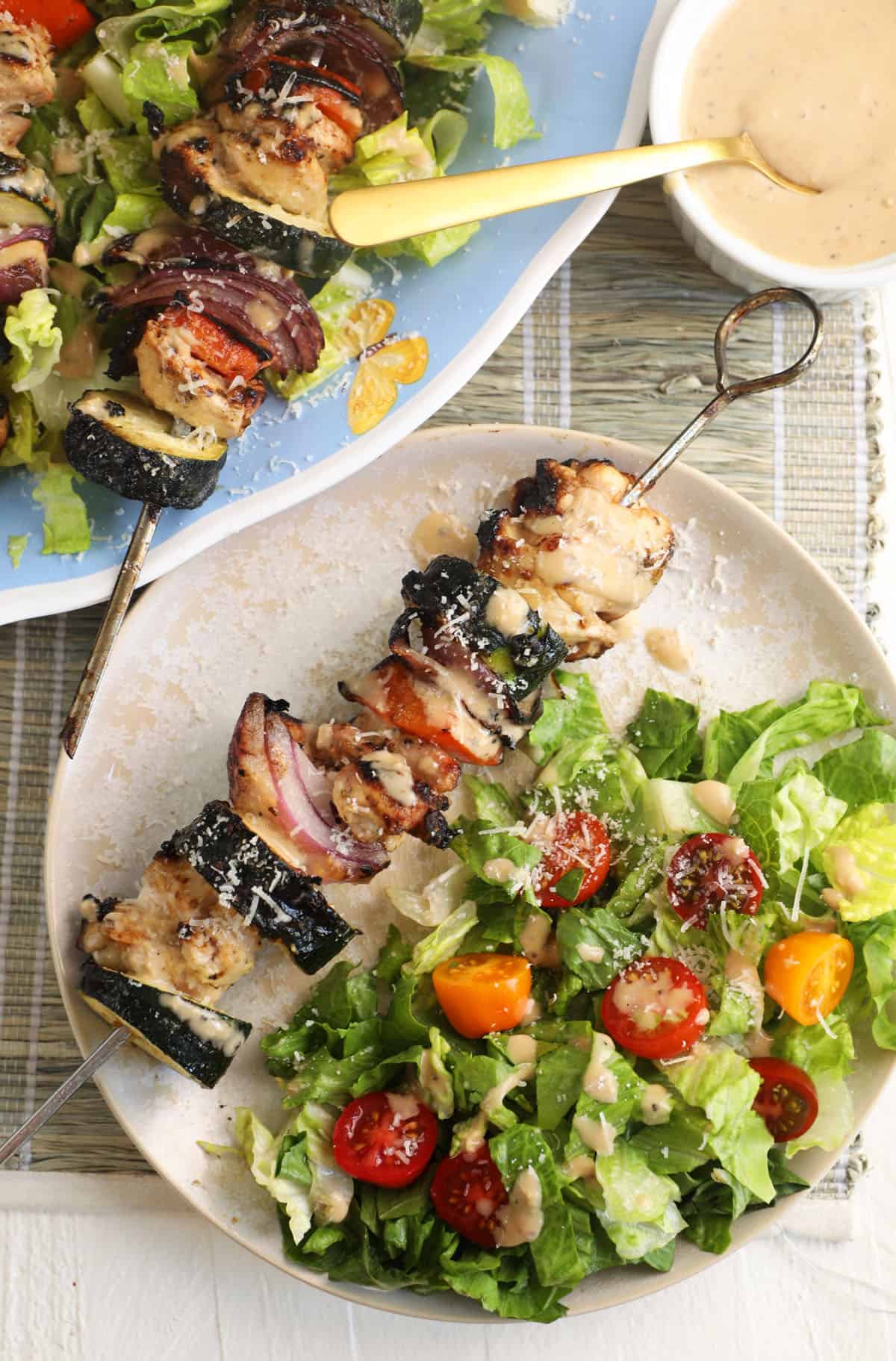 A chicken kabob is plated with a caesar salad. 