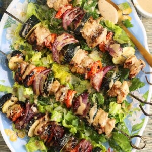 Four chicken kabobs are placed on a bed of lettuce.