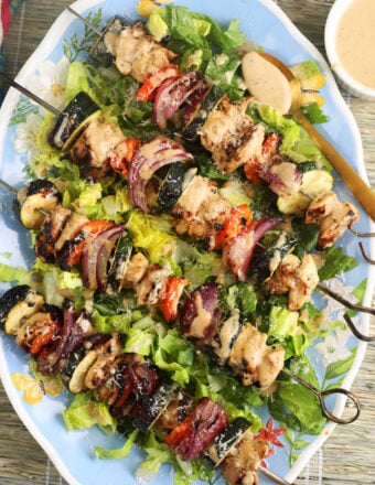 Four chicken kabobs are placed on a bed of lettuce.