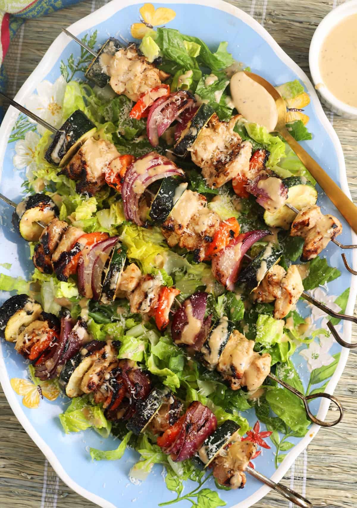 Four chicken kabobs are placed on a bed of lettuce. 