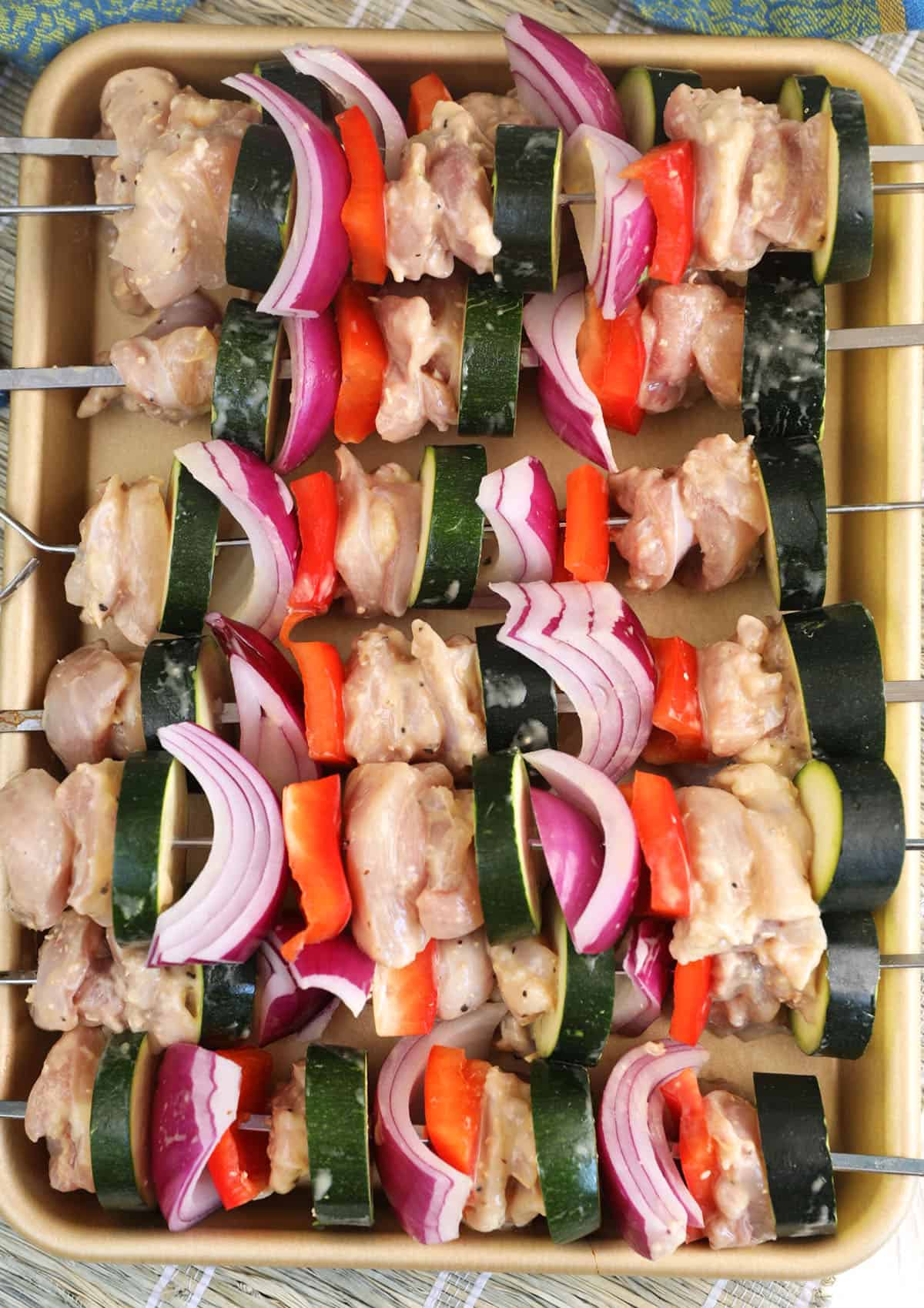 Uncooked chicken kabobs are placed on a baking sheet. 