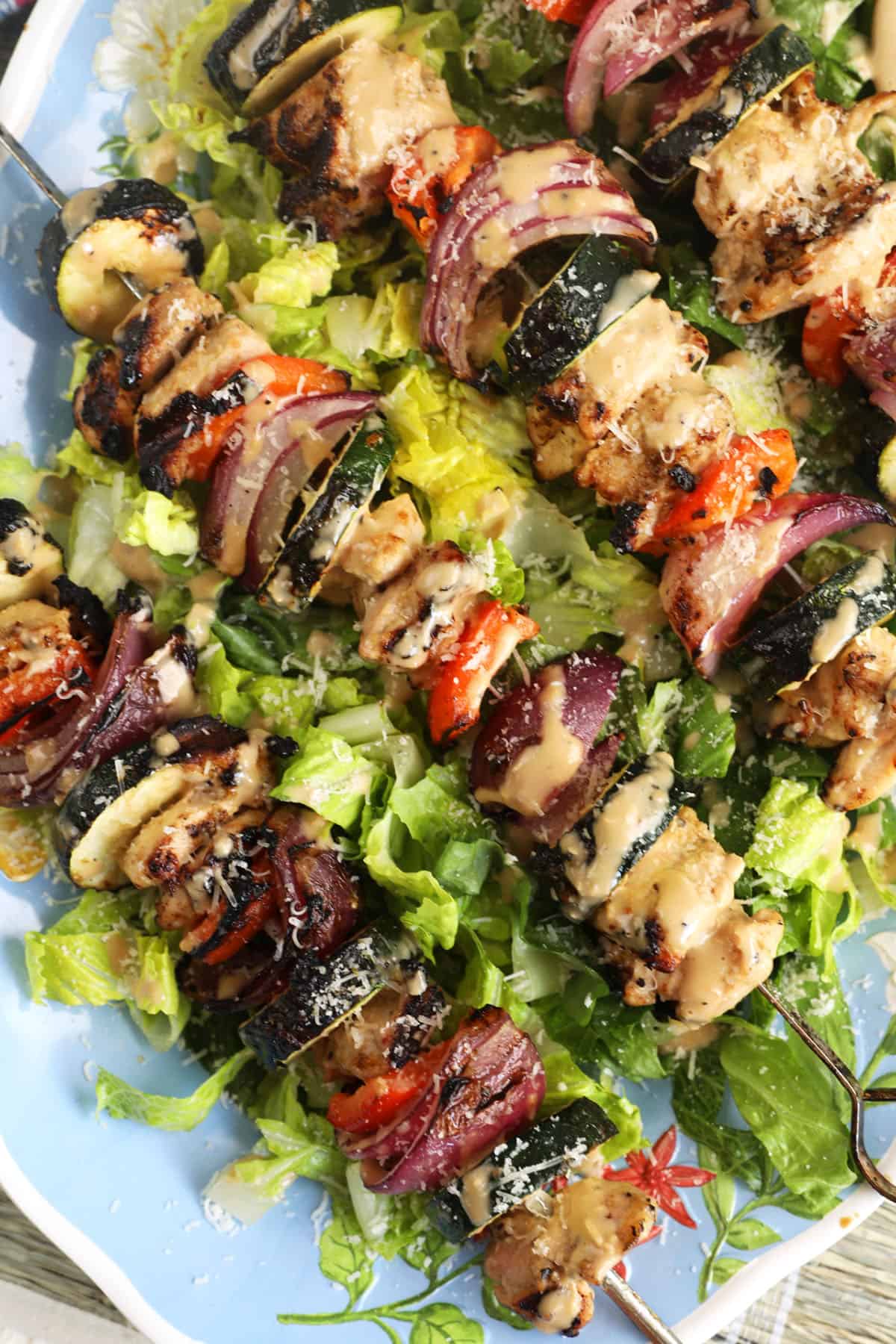 Several cooked kabobs are placed on top of a large bed of lettuce. 