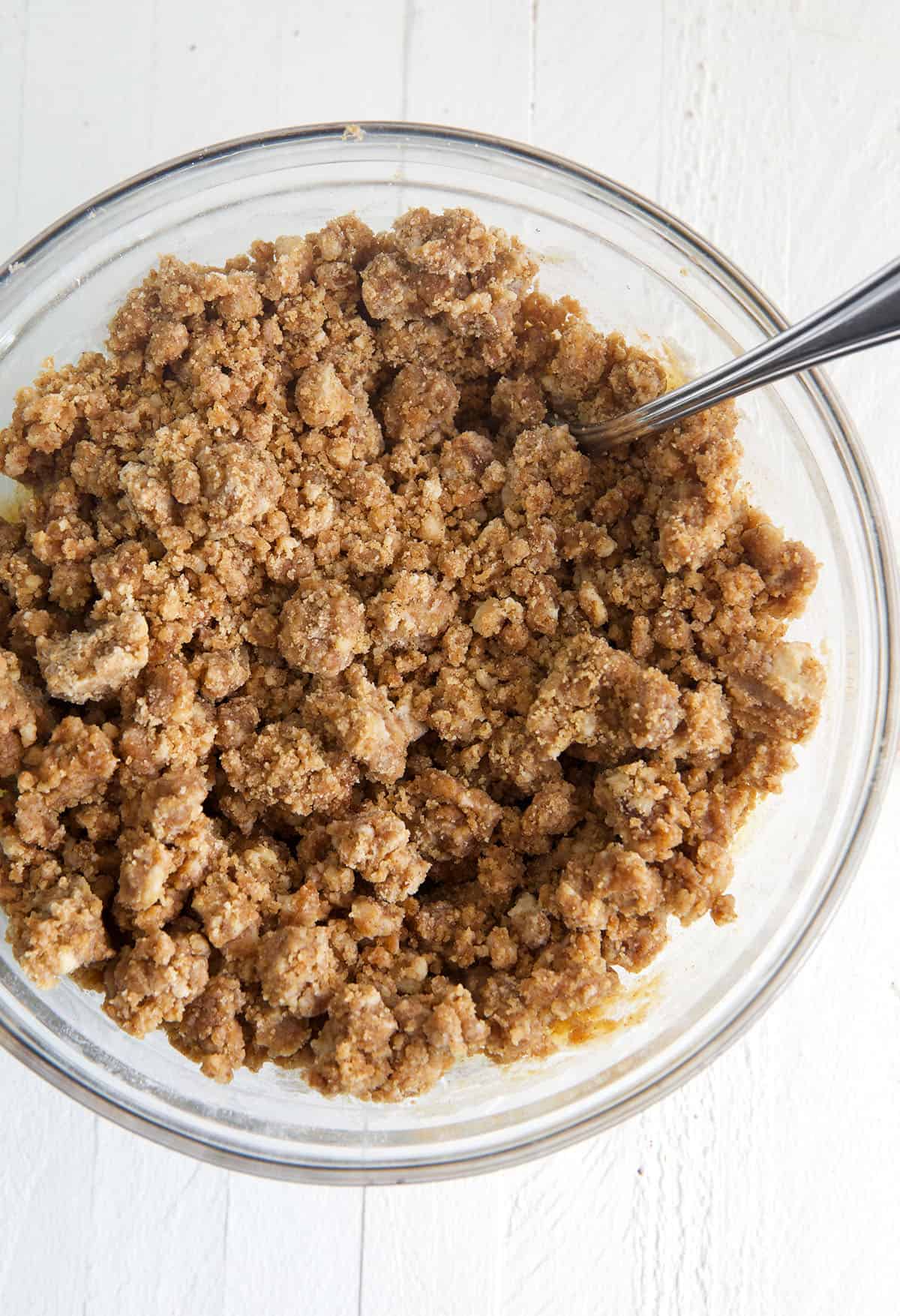 A small bowl of cinnamon crumb topping is presented with a spoon. 