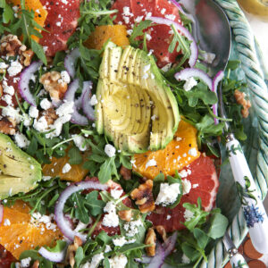 A large bowl of citrus avocado salad is presented with a serving spoon.