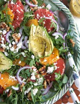 A large bowl of citrus avocado salad is presented with a serving spoon.