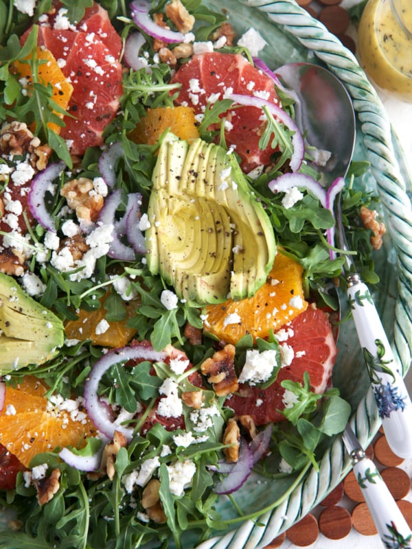 A large bowl of citrus avocado salad is presented with a serving spoon.