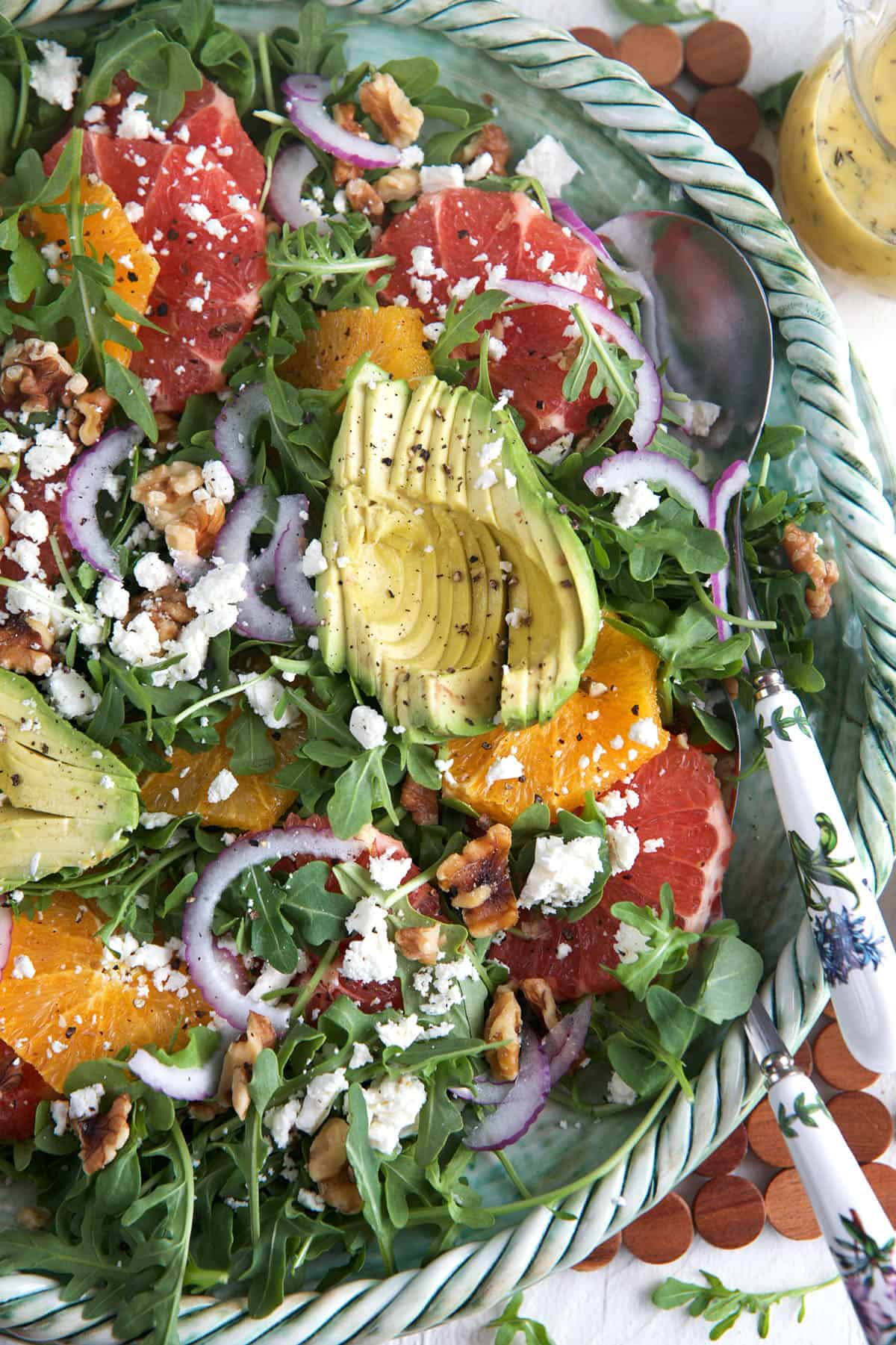 A large bowl of citrus avocado salad is presented with a serving spoon.