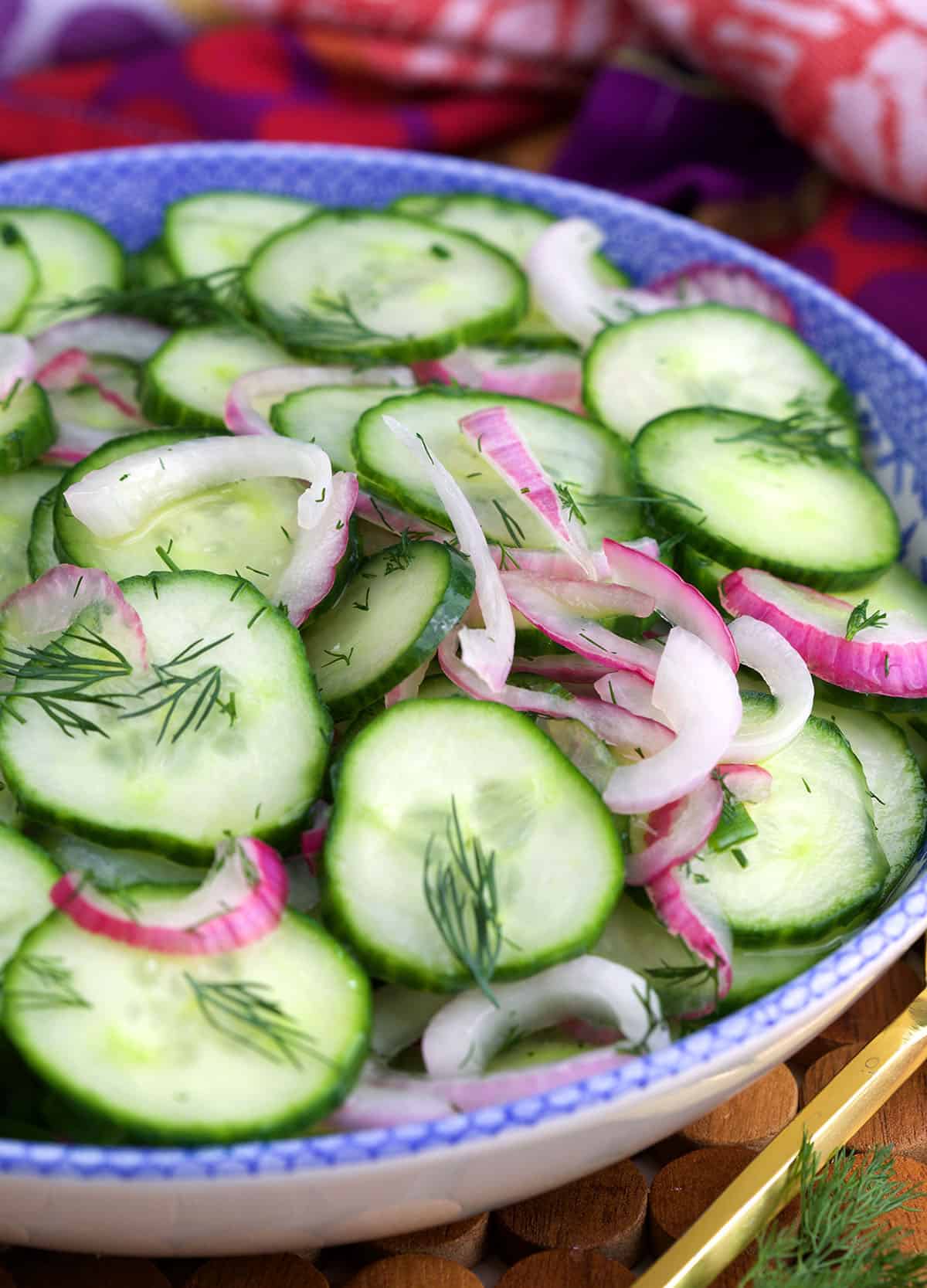 A bowl of cucumber onion salad is topped with fresh herbs. 