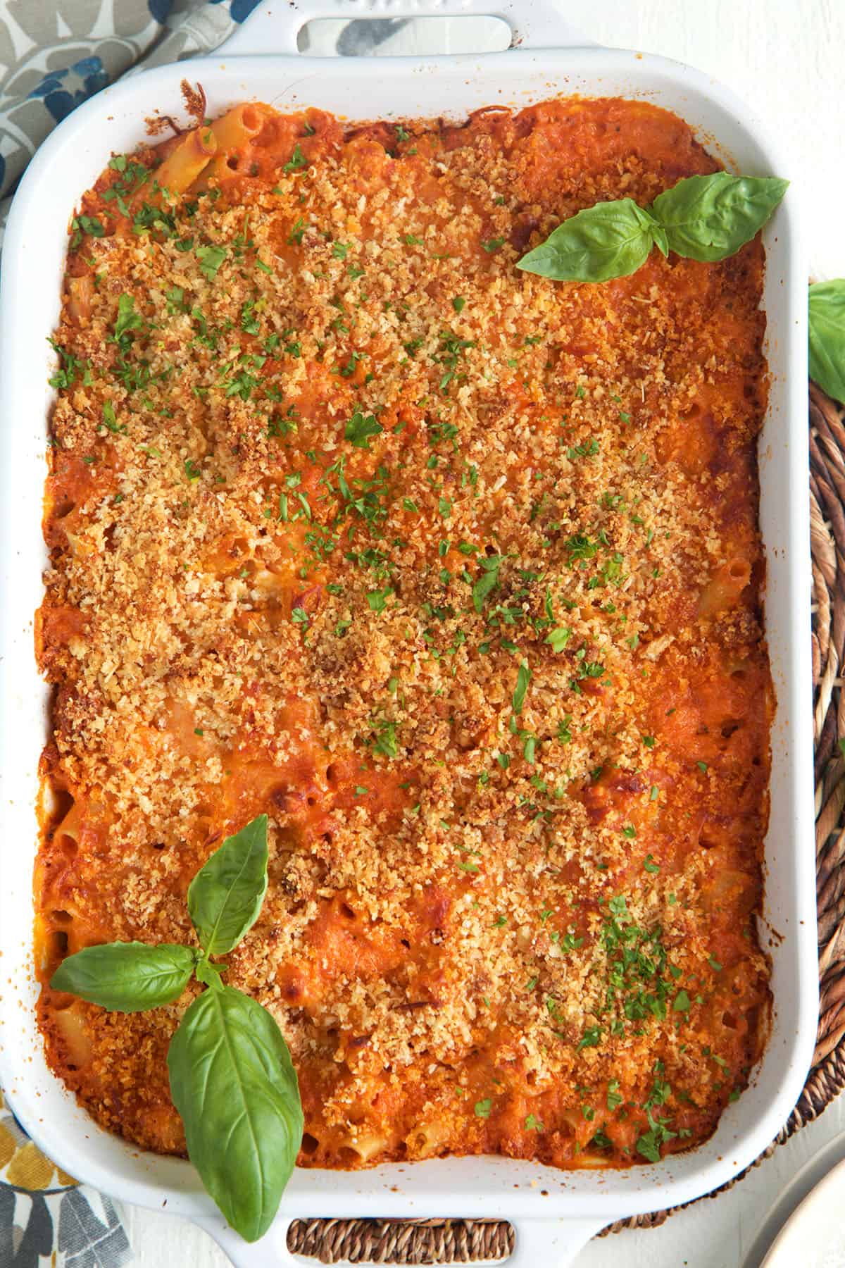 A white baking dish is filled with cheesy baked ziti. 