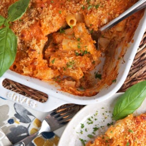 A plate is placed next to a casserole dish filled with baked ziti.