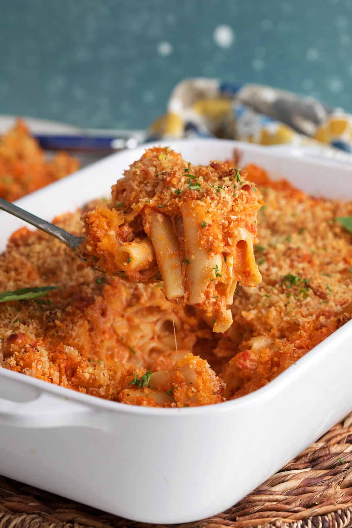 A spoonful of ziti is being lifted from a baking dish. 