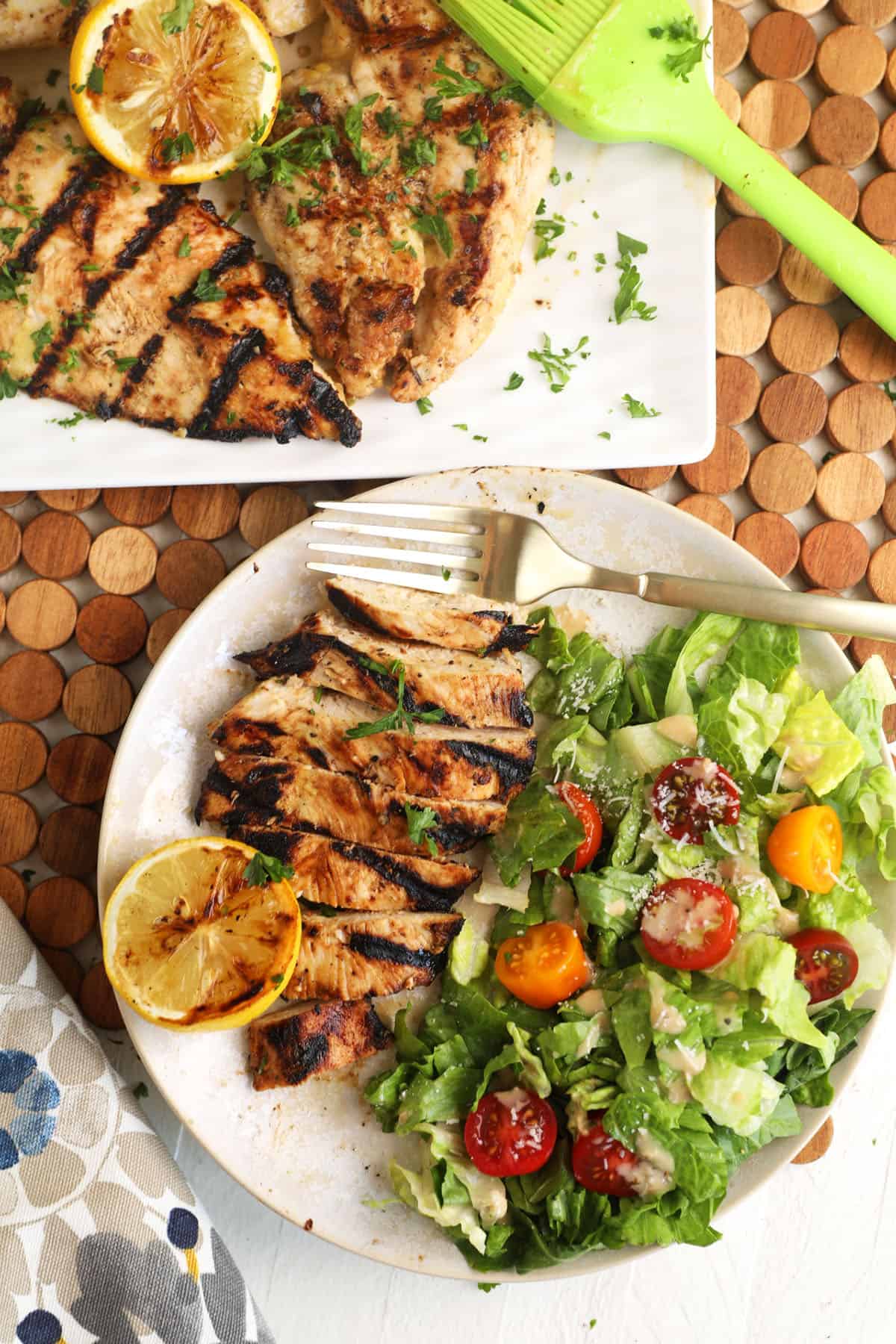 Salad, grilled lemon halves and chicken are on a white plate. 