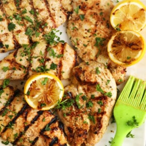 Grilled lemon chicken is presented on a white platter.