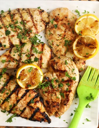 Grilled lemon chicken is presented on a white platter.