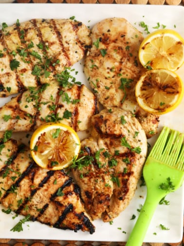Grilled lemon chicken is presented on a white platter.
