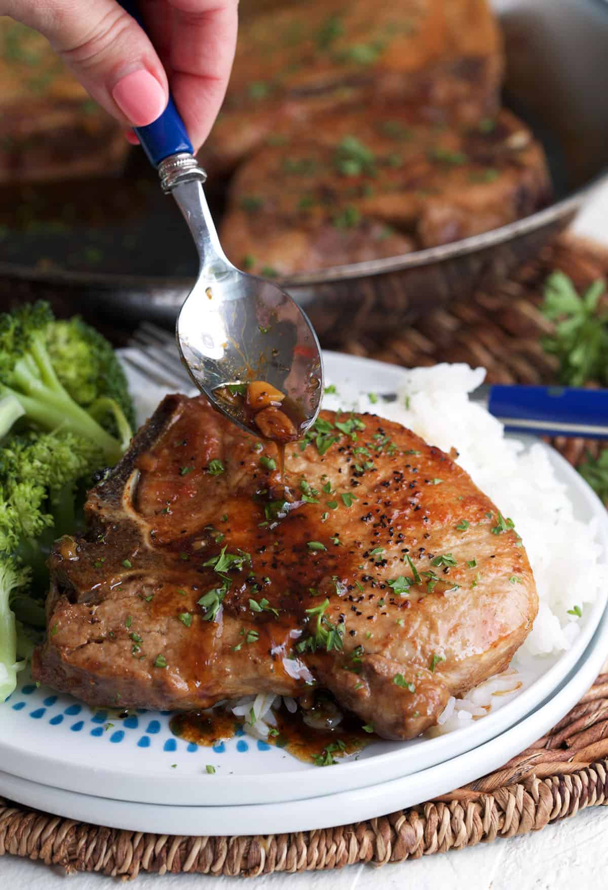 Pan sauce is being drizzled all over a cooked pork chop. 