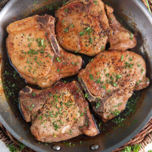 Four cooked pork chops are presented in a skillet.