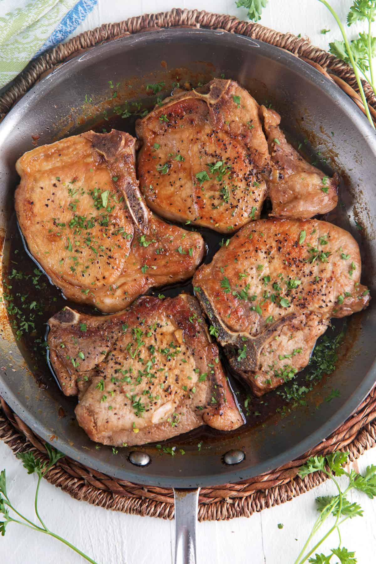 Four cooked pork chops are presented in a skillet. 