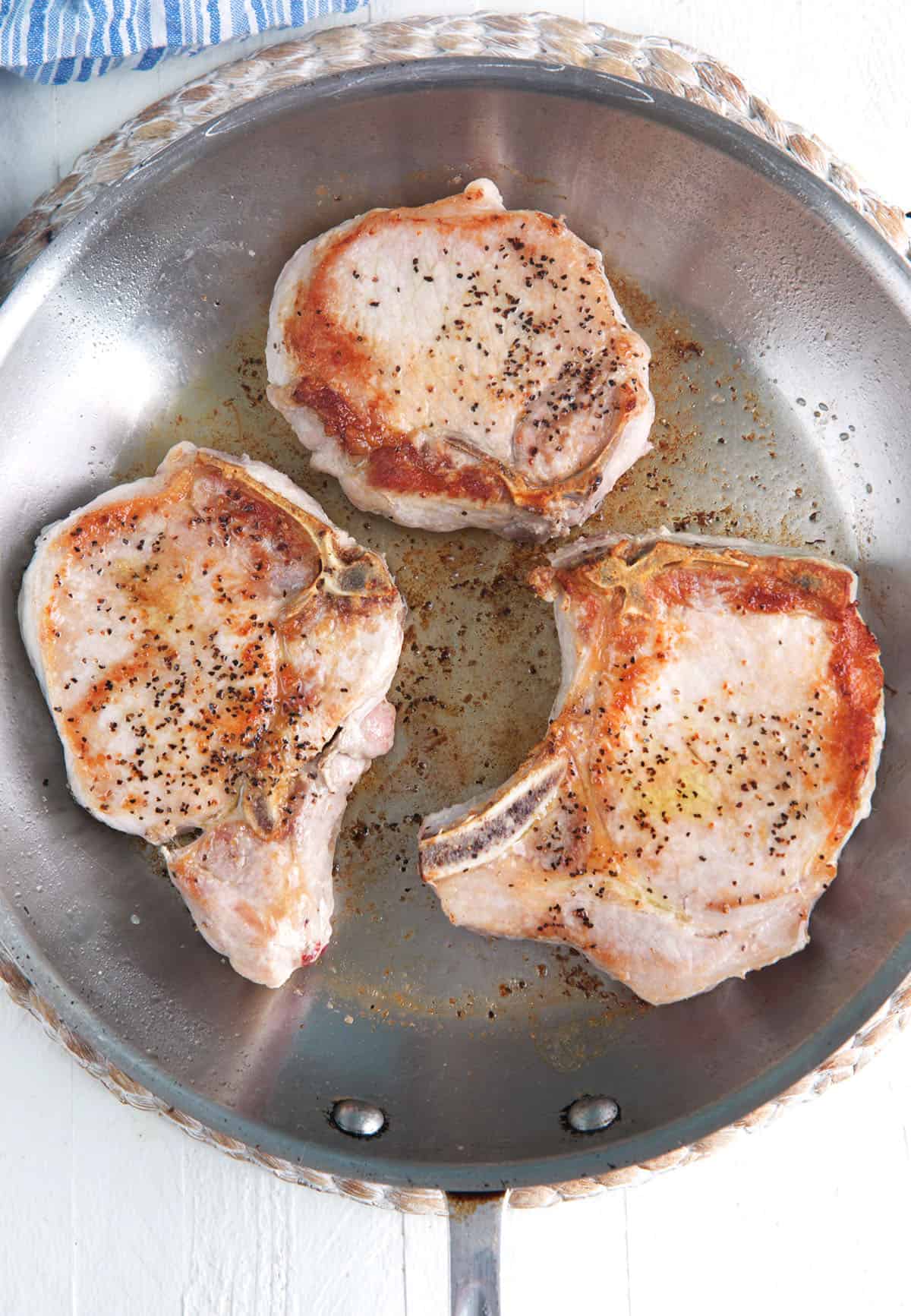 Three pork chops are being seared in a skillet. 