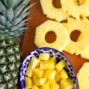 Slices and chunks of pineapples are placed next to a whole pineapple.