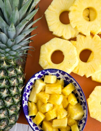 Slices and chunks of pineapples are placed next to a whole pineapple.