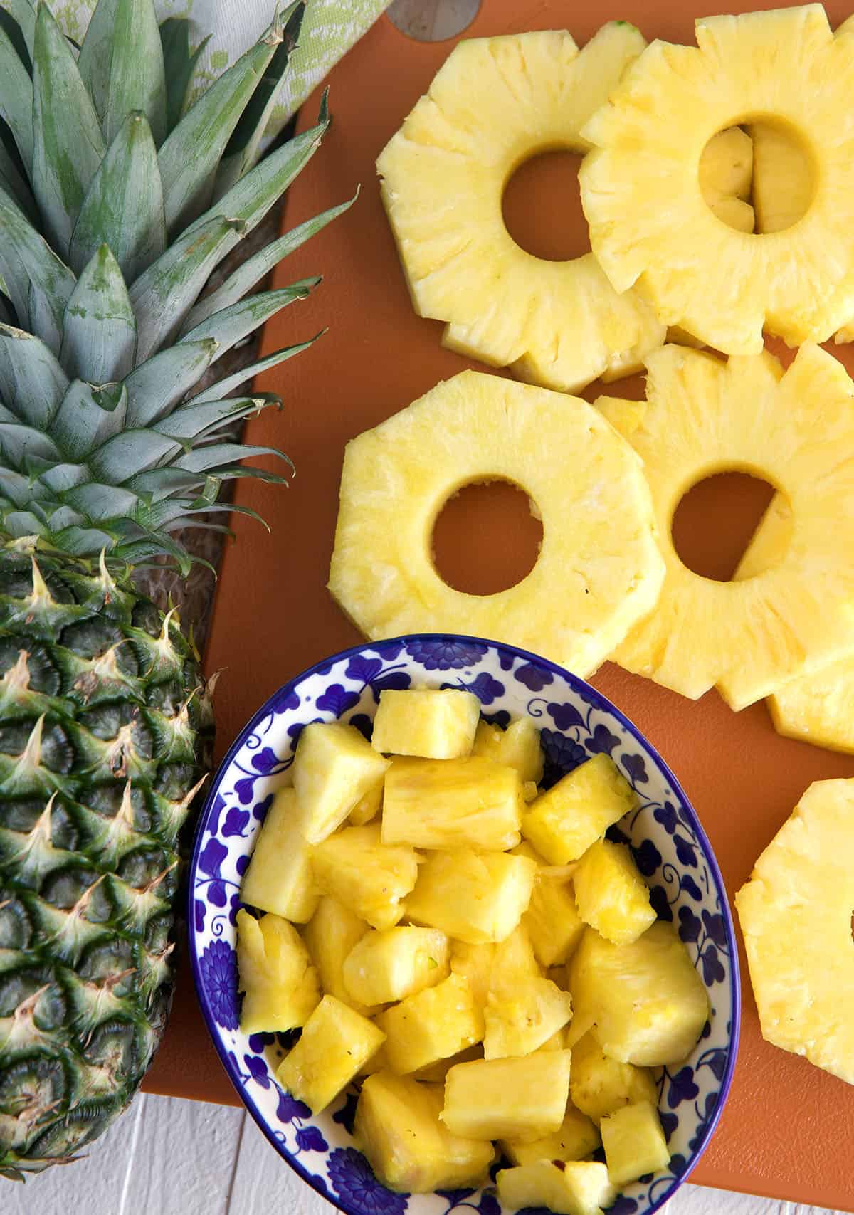 Slices and chunks of pineapples are placed next to a whole pineapple. 