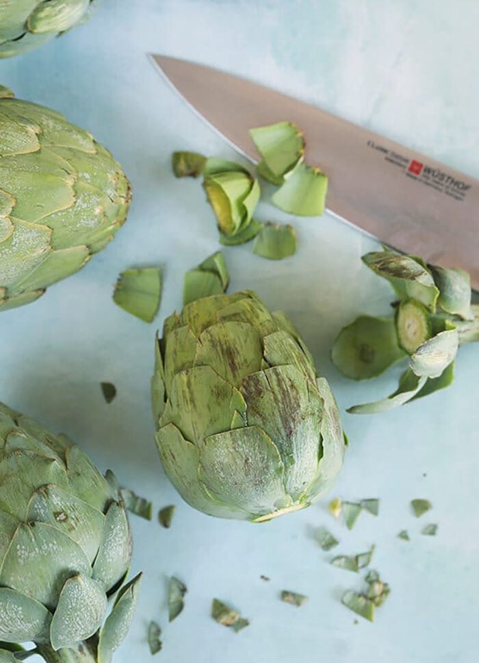 Artichoke on a blue board with the top and bottom cut off ready to be cooked.