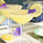 Two martinis are placed on a white plate with garnishes.
