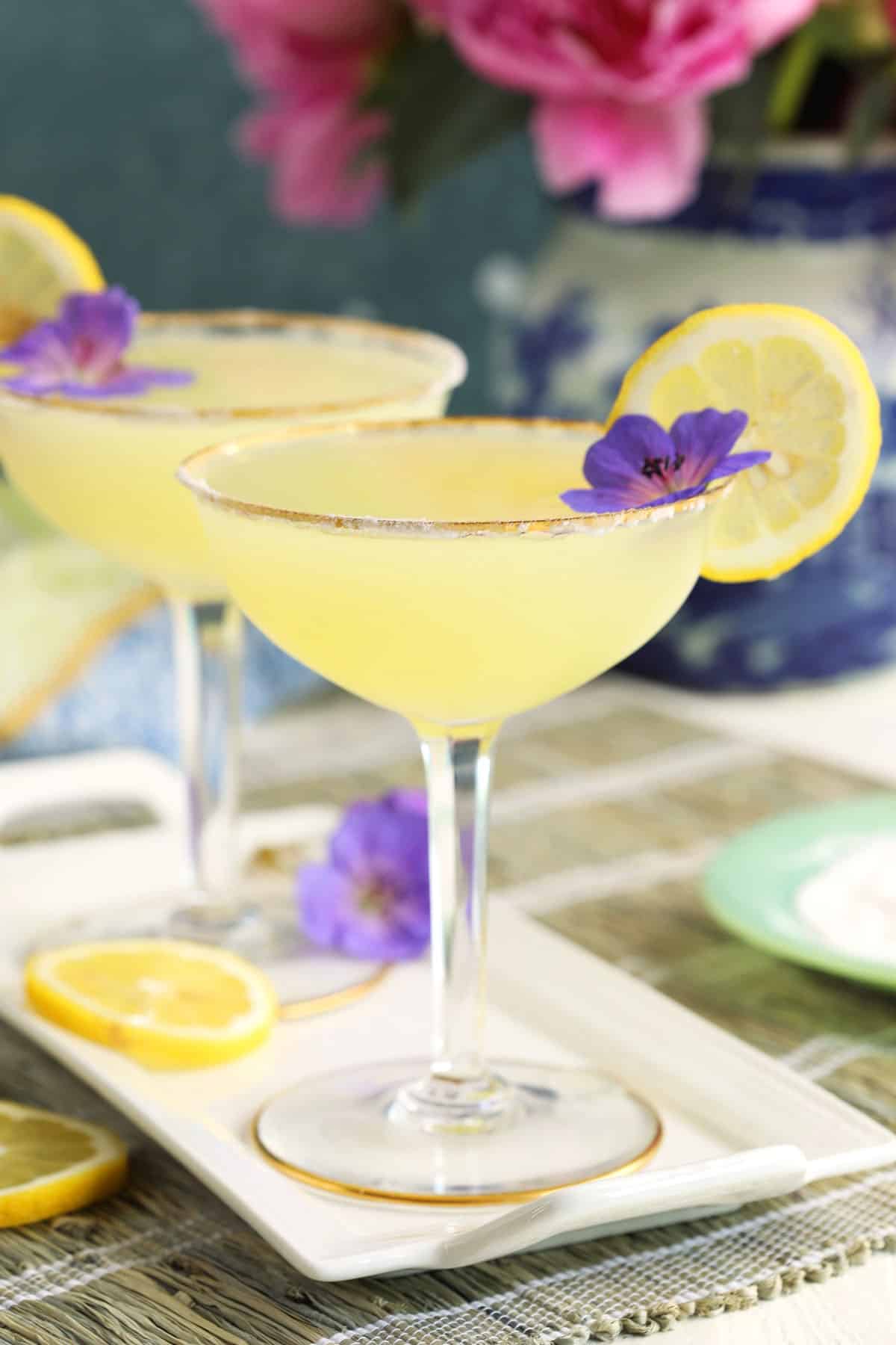 Two martinis are placed on a white plate with garnishes. 