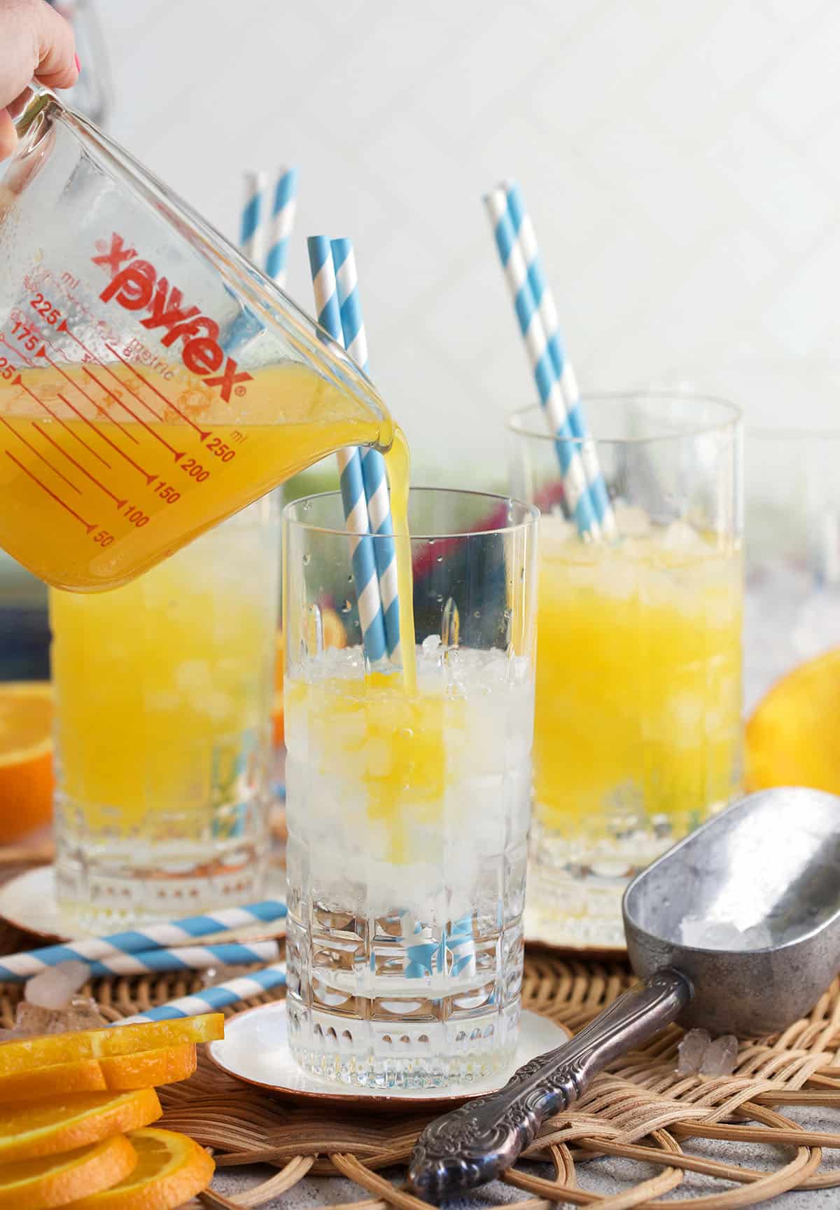 Orange juice being poured over ice in a collins glass.