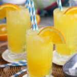 Orange Crush Cocktail in a collins glass with an orange wedge on the side and blue and white striped straws.